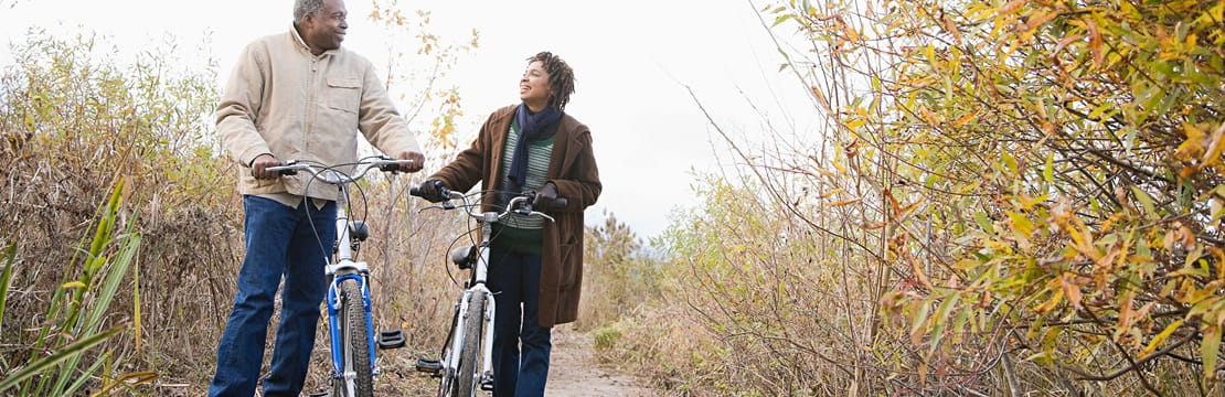 Mature couple pushing bicycles on a nature trail.